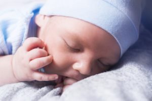Mały śpiący noworodek ubrany w błękitną czapkę i śpioszki.